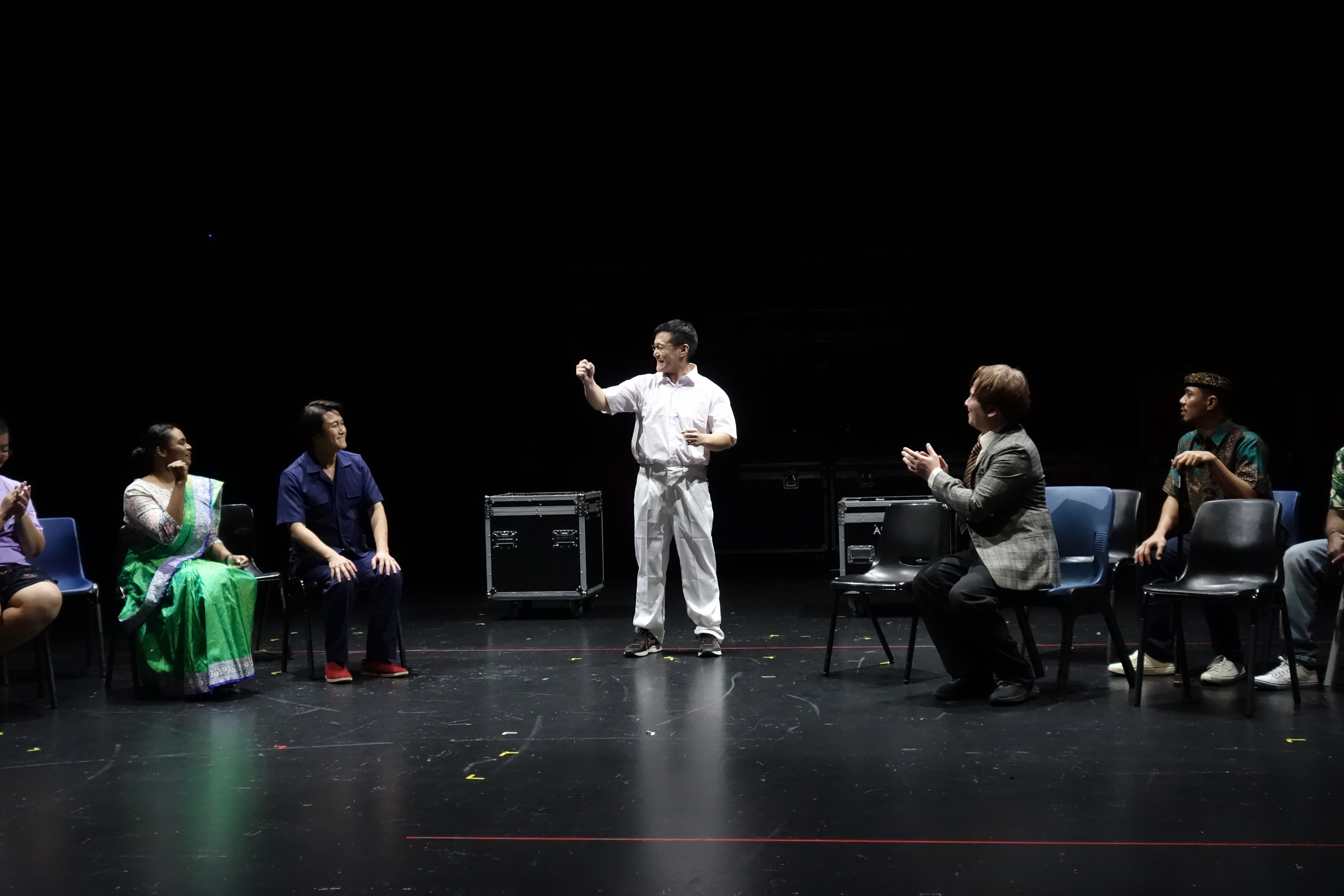 Wide shot of Director Ngeow speaking to the cast members in a scene