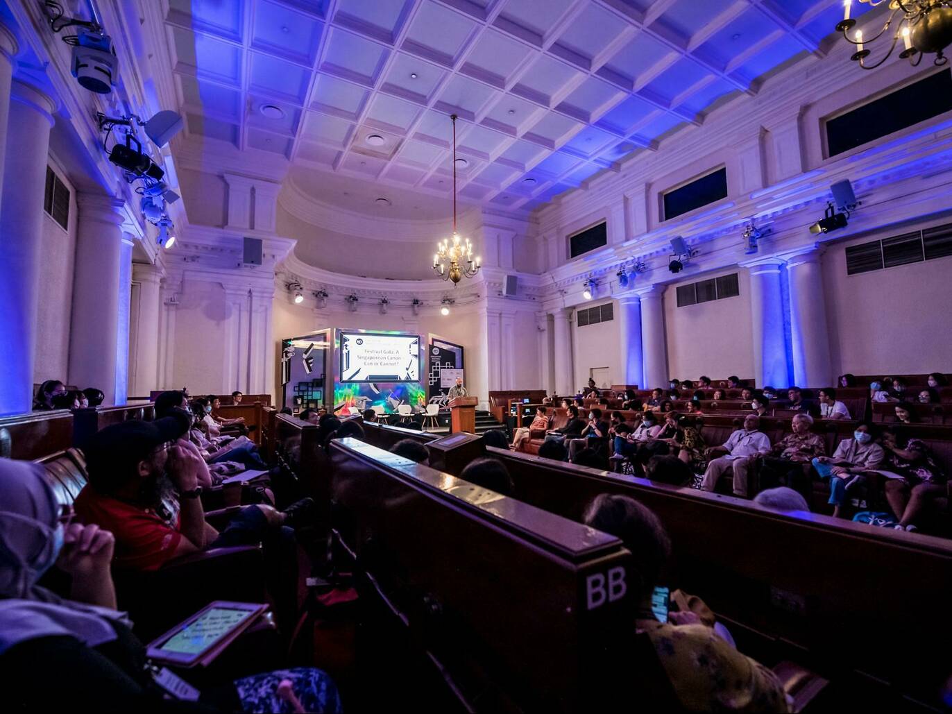 Wide shot of people gathered within a neon-lit hall