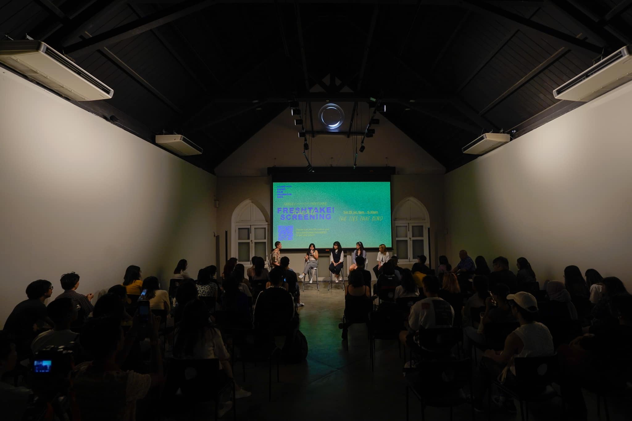 Wide shot of a crowd gathered for a screening with a panel of speakers