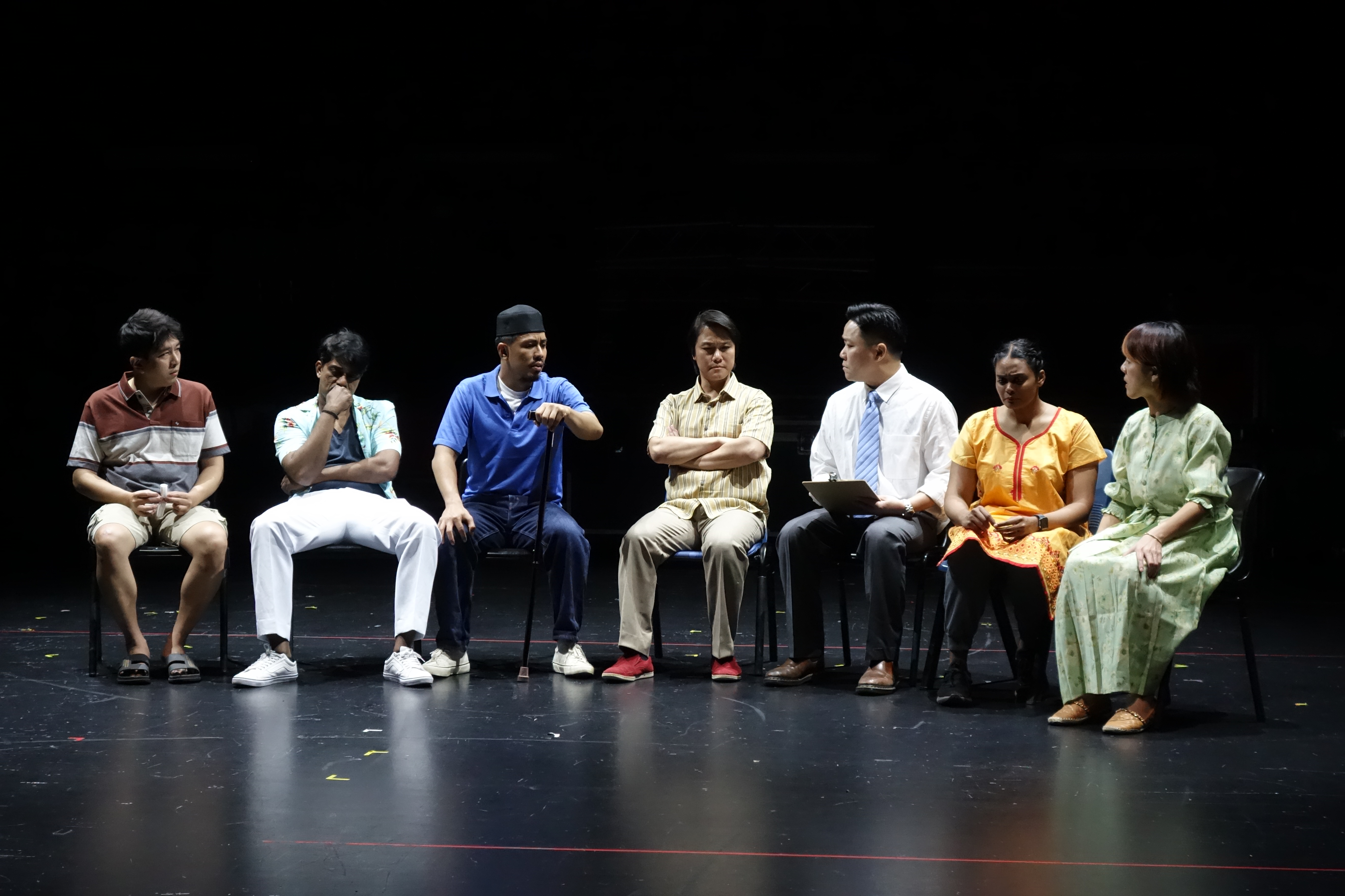 Wide shot of cast sitting in a row during a therapy session scene
