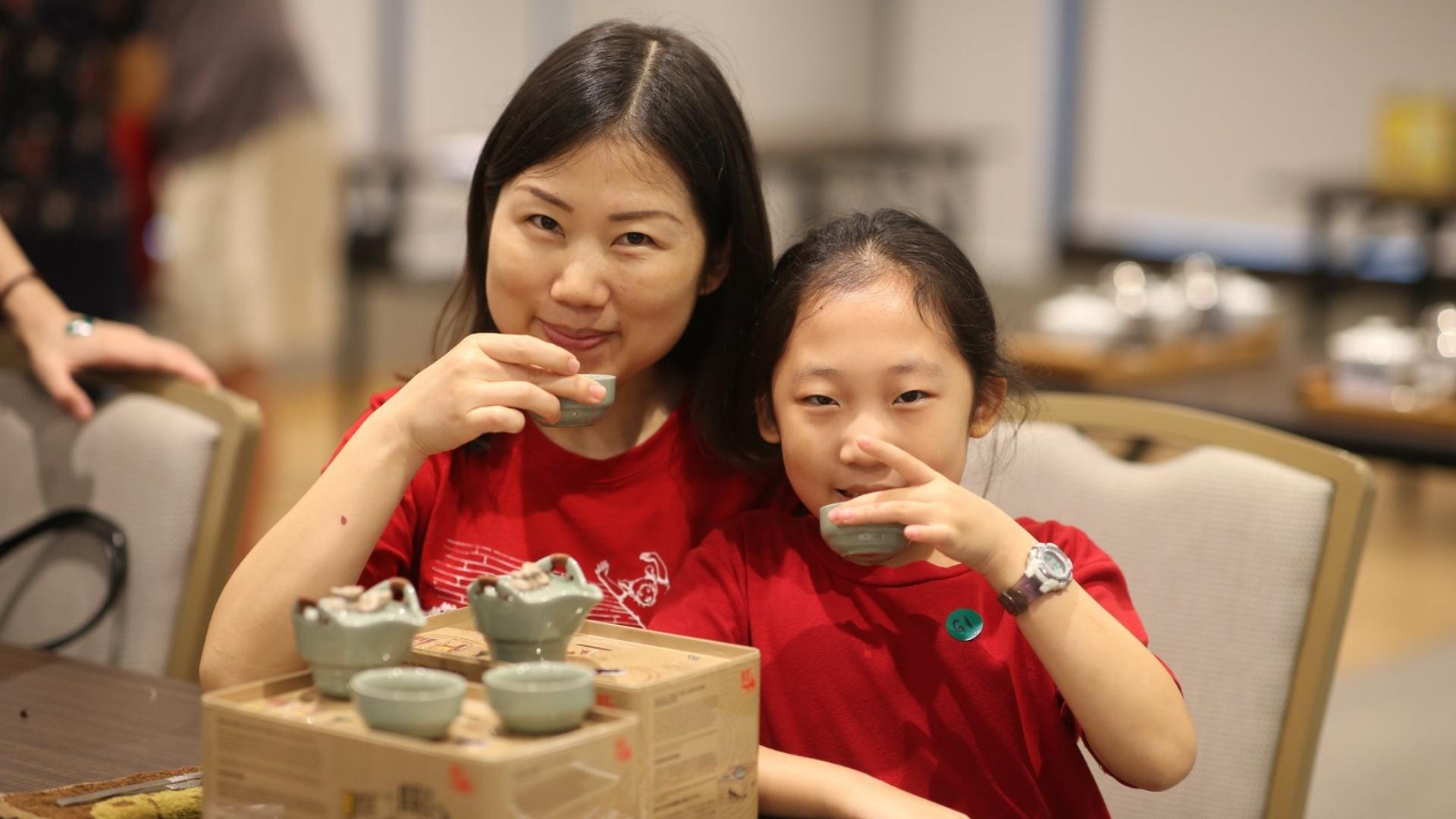 Mid shot of a child and her mother drinking traditional chinese tea.