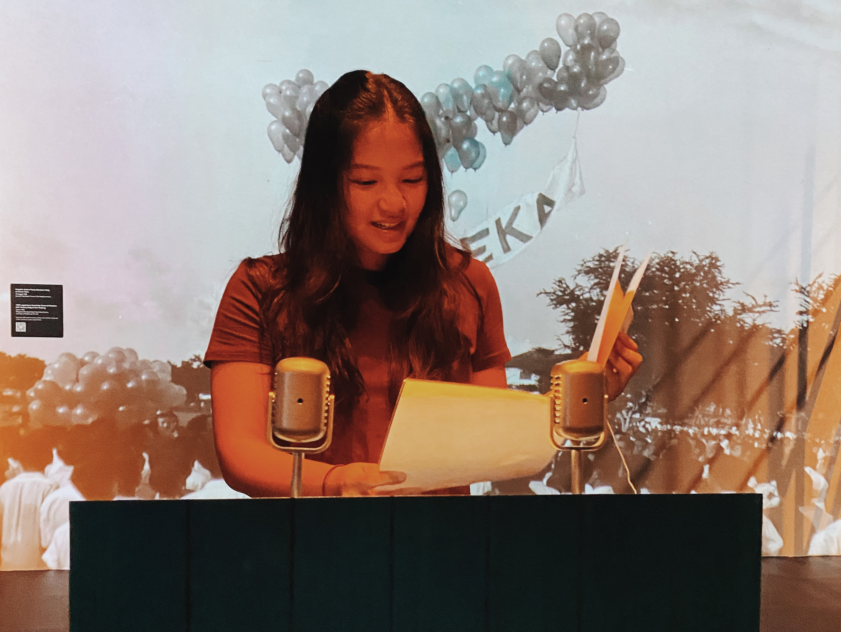 Close-up of a young woman standing at a podium, reading off papers