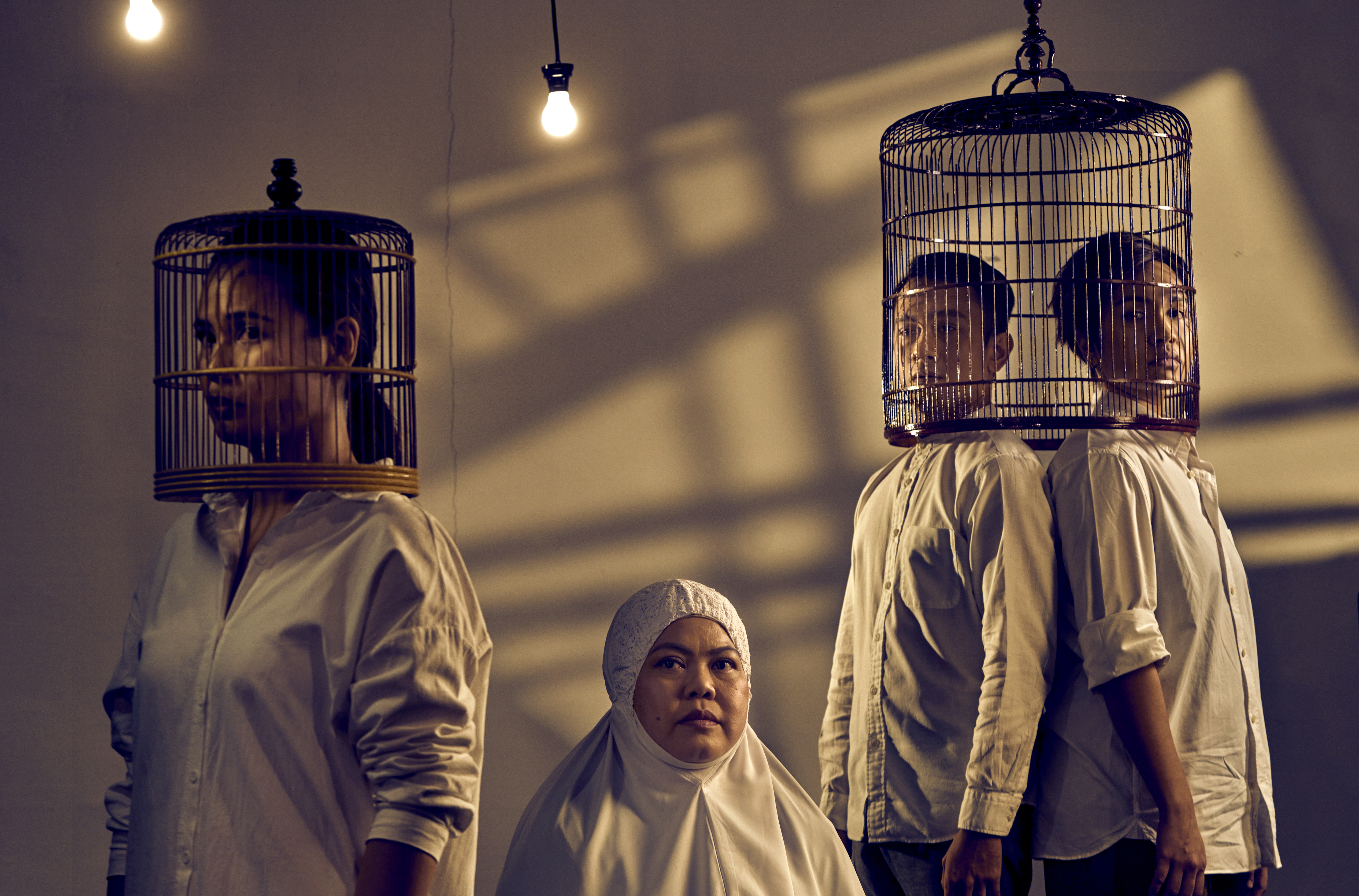 Three persons wearing bird cages over their heads, and a lady in a Malay prayer garment