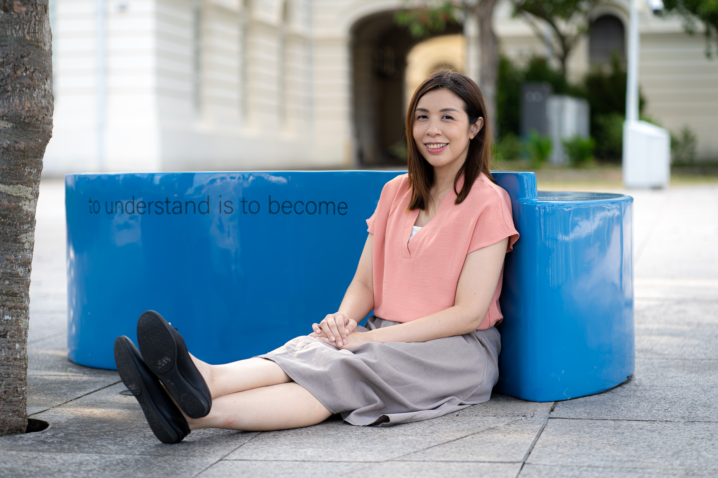 Wide shot of Laura Kee sitting on the ground and leaning against artwork A Micropolyphonic Stage