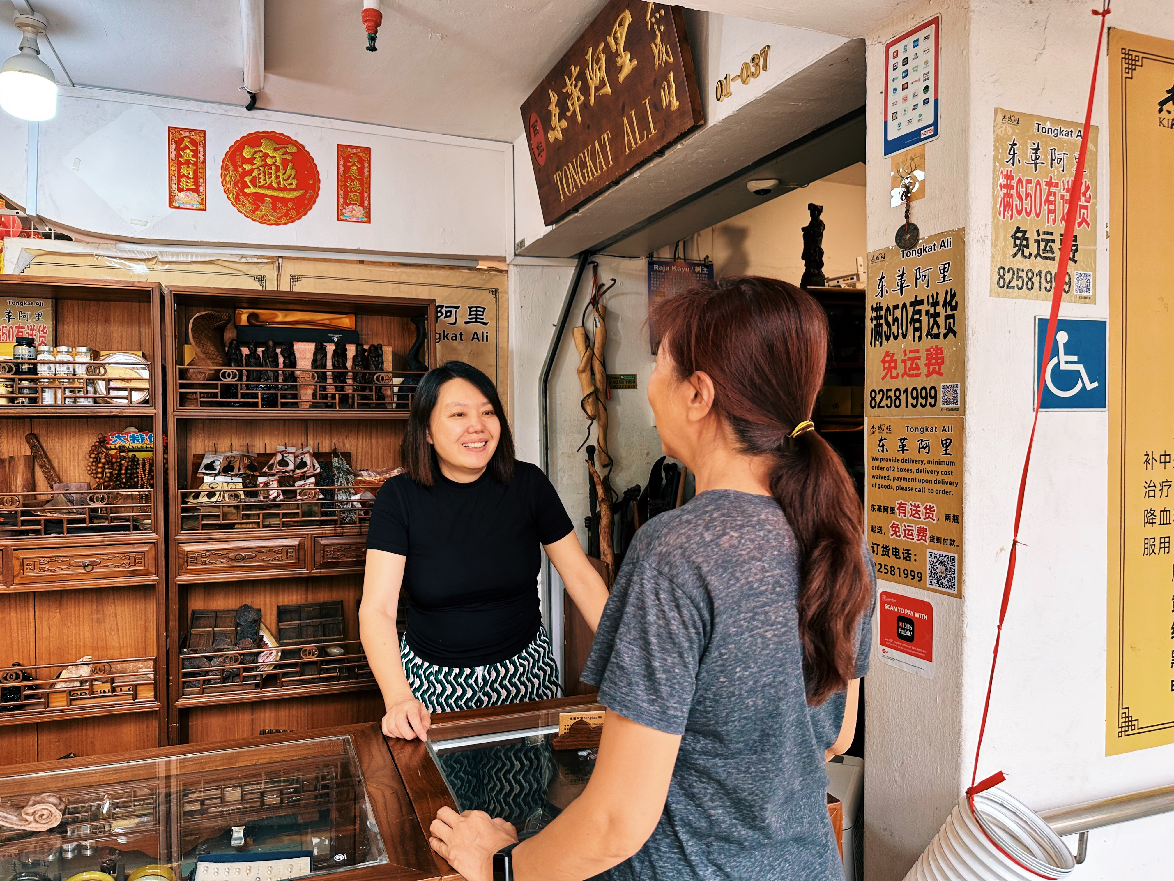 Wide shot of attendee talking with seller of the traditional “tongkat ali” aphrodisiac Yilin Wang over the counter