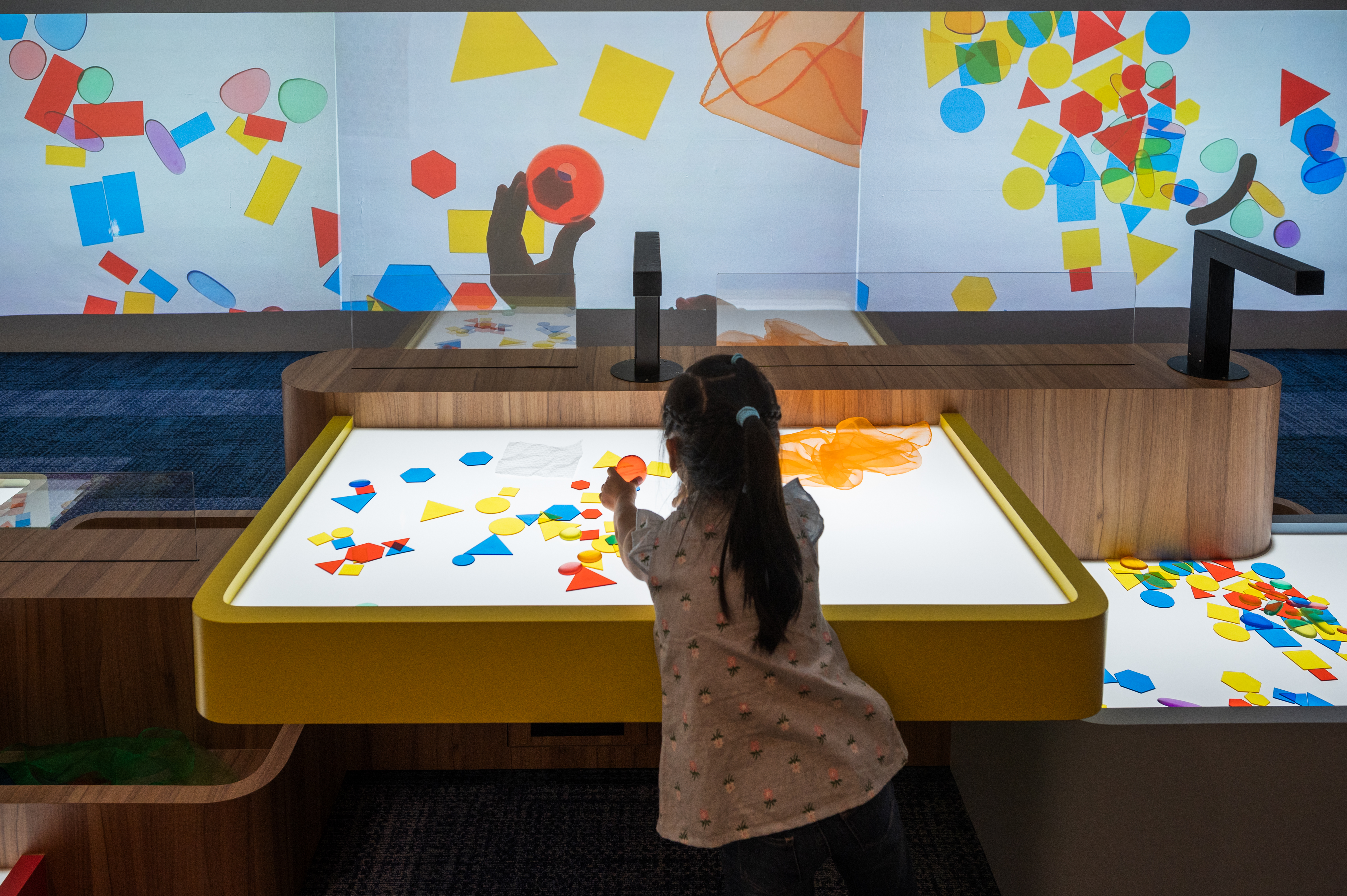 Wide shot of a young girl engaging with an exhibition play area in the Illuminate! zone