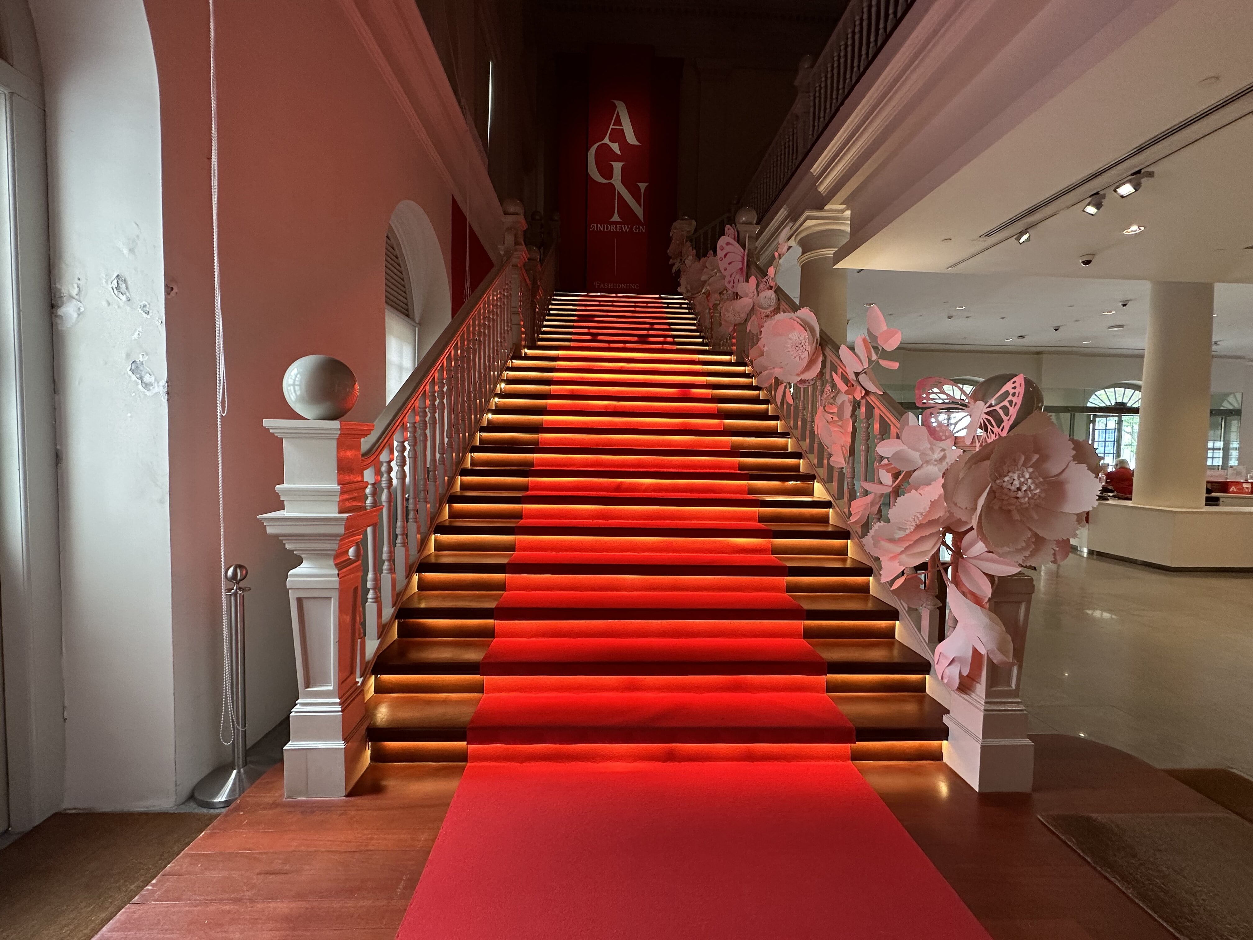  Wide shot of a red carpeted staircase leading up towards the Andrew Gn exhibition