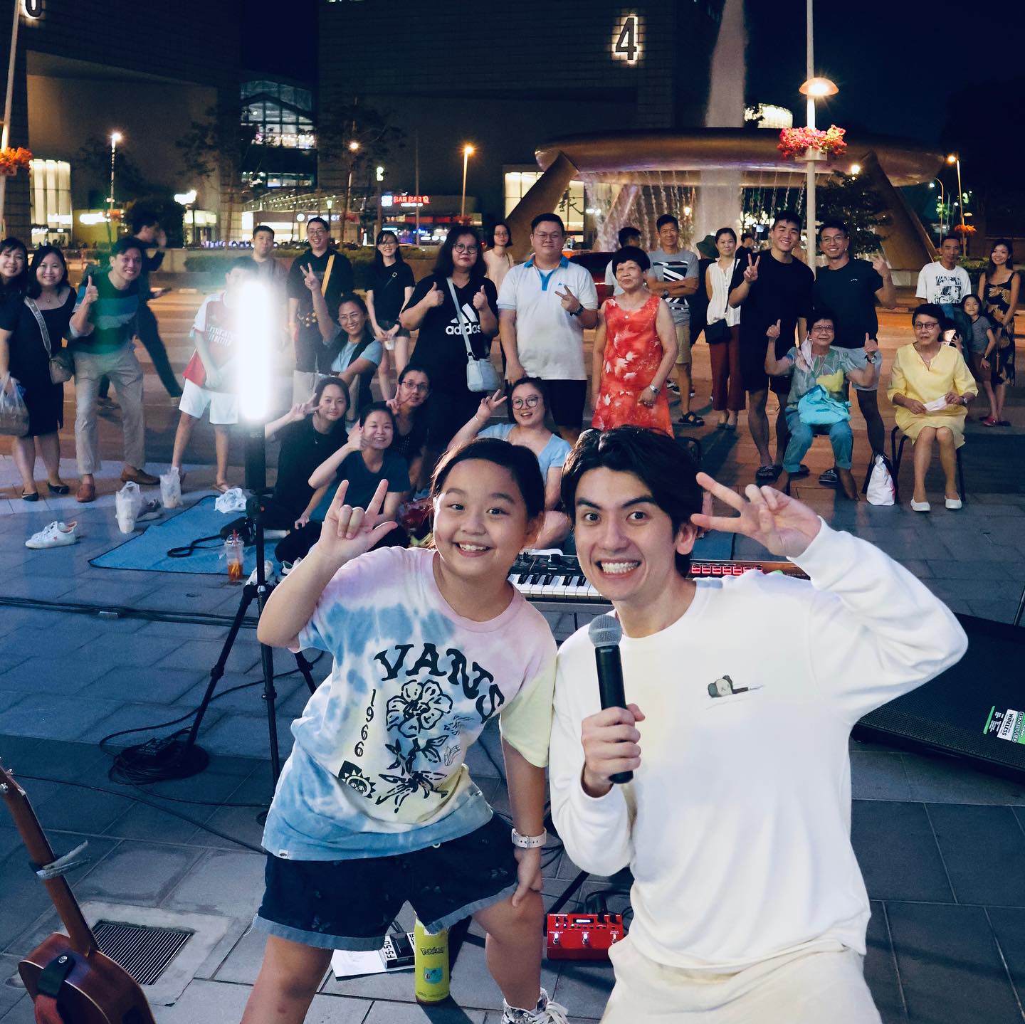 Wide shot of Lyla Ng posing with Sheng Li and an audience at a busking spot
