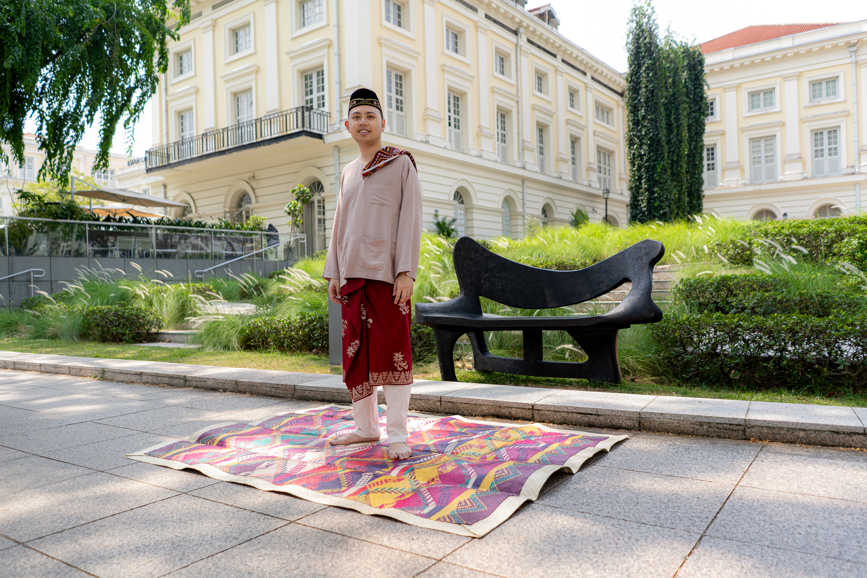 Wide shot of Haifz Rashid standing on top of a rug in front of artwork Re-Store / Neutral Artefact Black