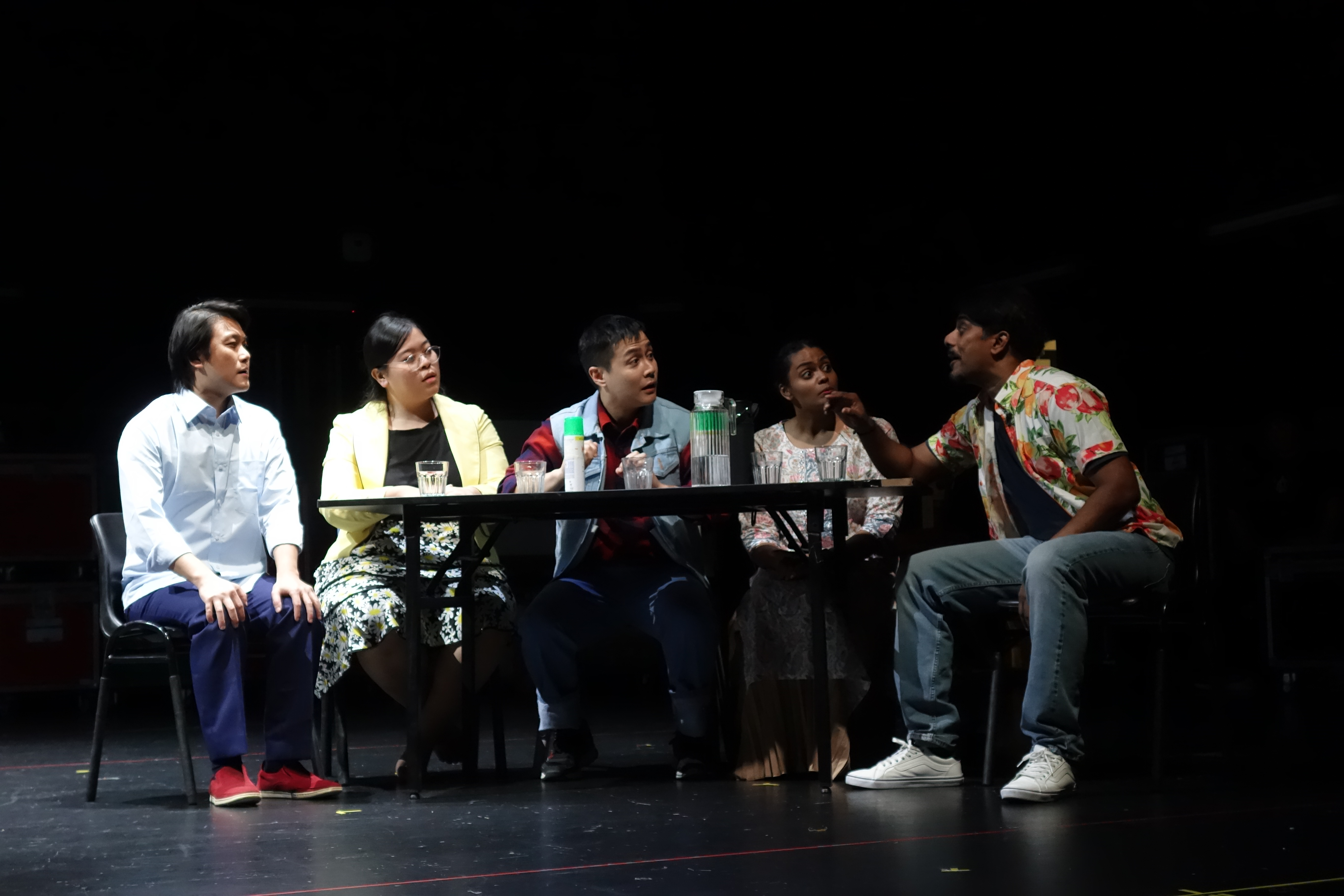 Wide shot of cast members communicating at a table